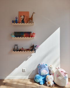A child's bedroom with stuffed animals on the floor and shelving to hold small items